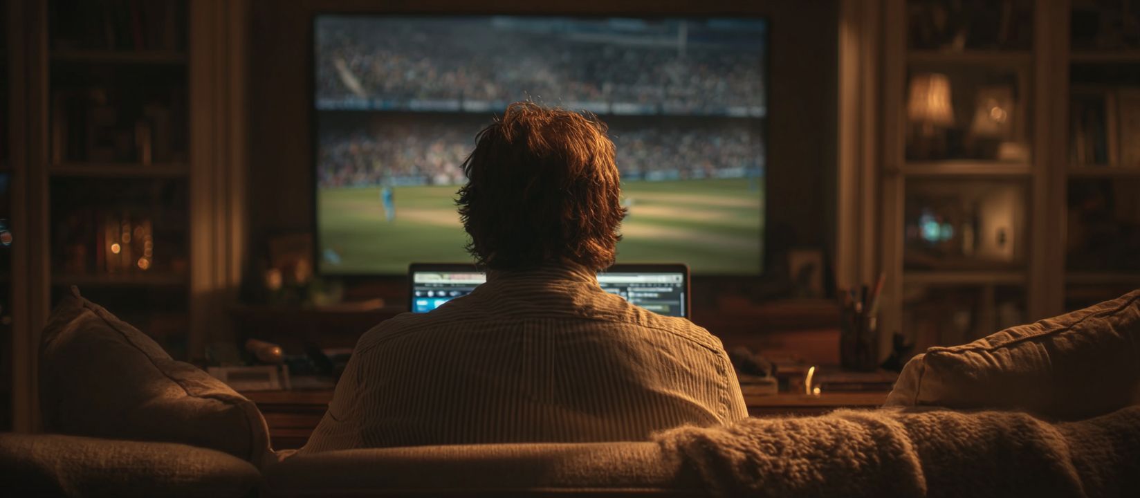 Man watching cricket on TV while placing live bets on Kikriya platform from his laptop